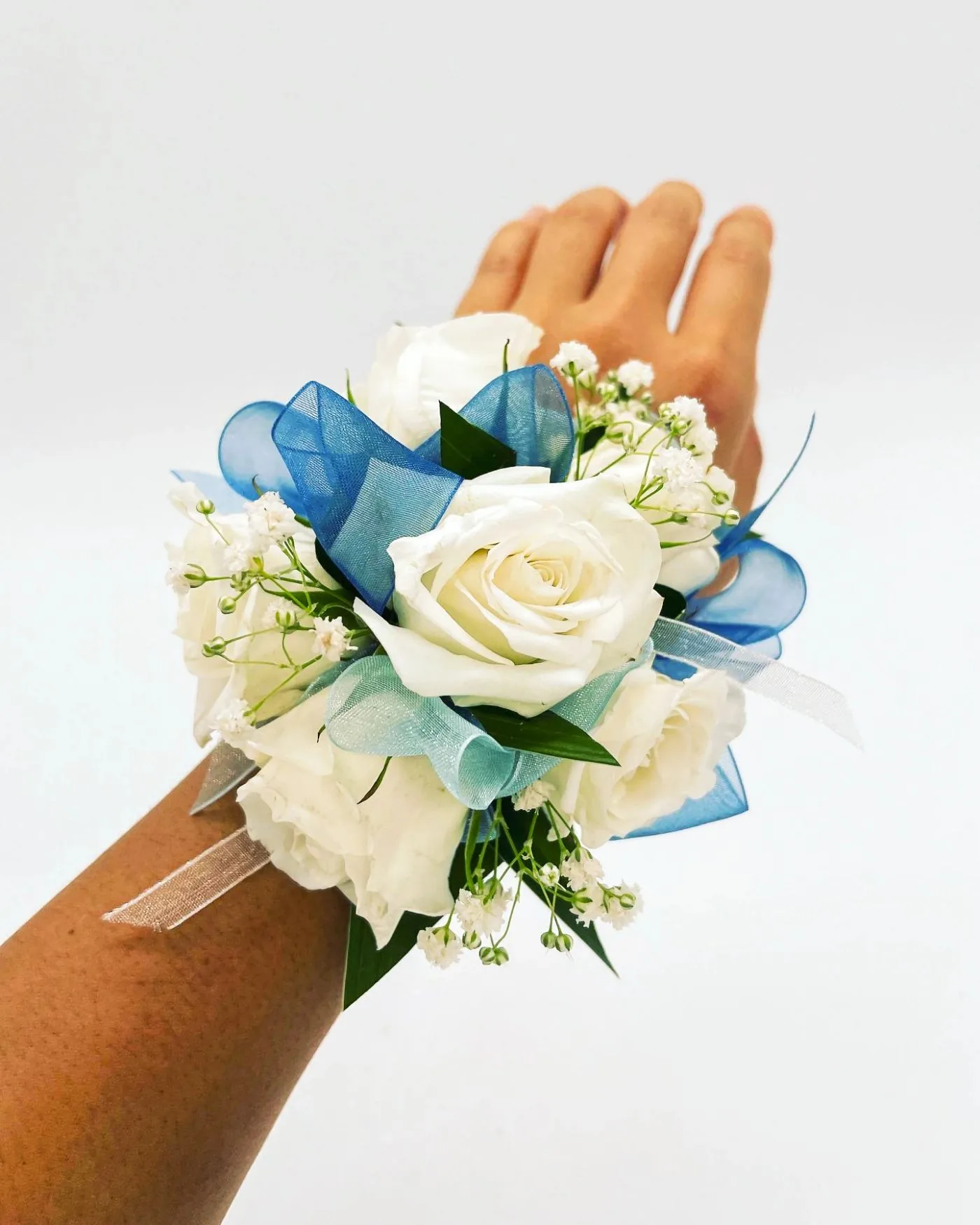 A white rose wrist corsage tied with blue organza ribbon, worn on a wrist.