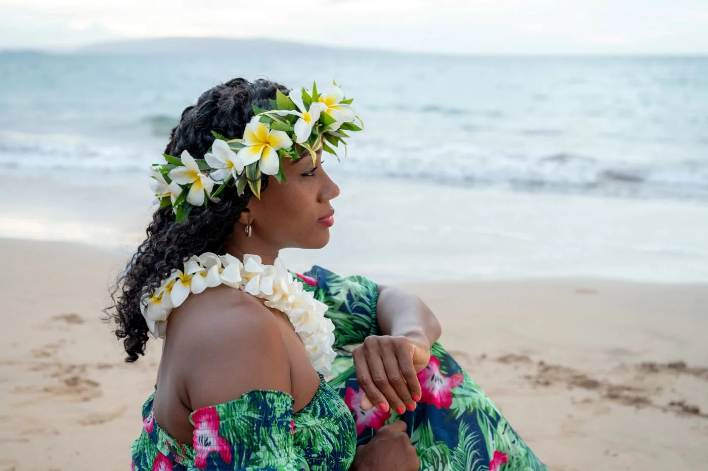 A woman on the beach wearing a plumeria haku flower crown and a white plumeria lei.