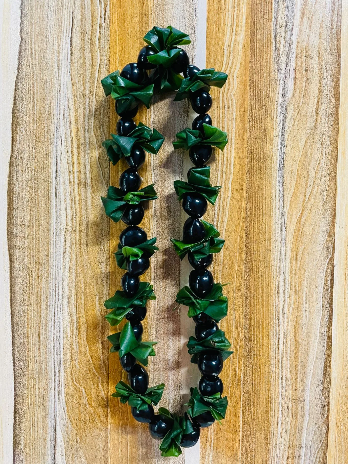 A glossy black kukui-nut graduation lei accented with green ti-leaf twists.